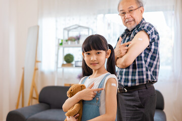 Senior man after vaccination and  granddaughter at home. Virus protection. COVID-2019.Vaccination in the shoulder of child patient  at home.