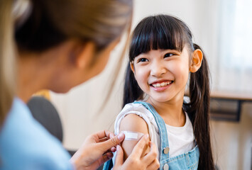 Childhood vaccination. Asian young woman doctor vaccinating little girl at home. Vaccine for...