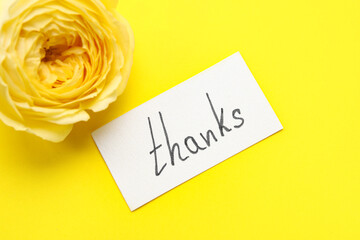 Sheet of paper with word THANKS and flower on yellow background