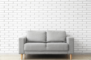 Grey sofa near white brick wall