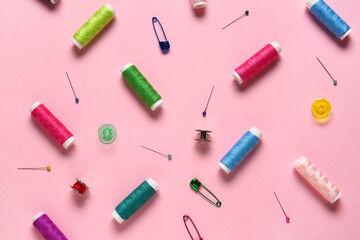 Thread spools and ball pins on pink background