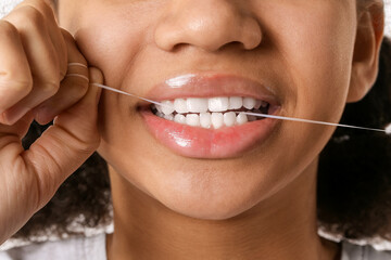 African-American teenage girl flossing teeth on white background, closeup
