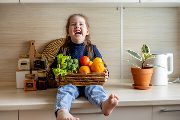 Baby sits on the kitchen table and holds a wicker basket of fruit in her hands.