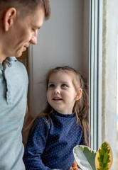 Father and daughter are standing near the window in the kitchen. Time spent together.