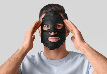 Handsome man with black facial mask on grey background