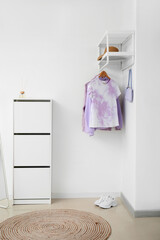 Rack with stylish clothes and chest of drawers near light wall