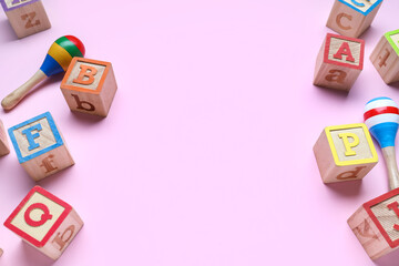 Wooden cubes with letters and rattles on pink background