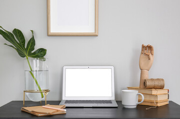 Laptop with plant leaf in vase, wooden hand and cup on table near white wall