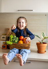 Baby sits on the kitchen table and holds a wicker basket of fruit in her hands.