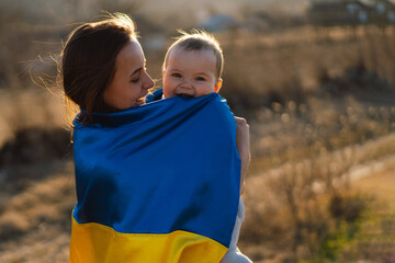 Woman hugs her little son wrapped in yellow and blue flag of Ukraine in outdoors. Independence Day....