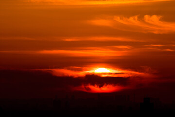 Sunset over the city. Orange sky and sun behind the clouds.