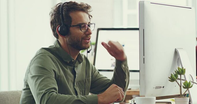 Working to find you a solution. Handsome cheerful young caucasian male call center support agent working on his computer while wearing a headset listening to customers and trying to solve problems