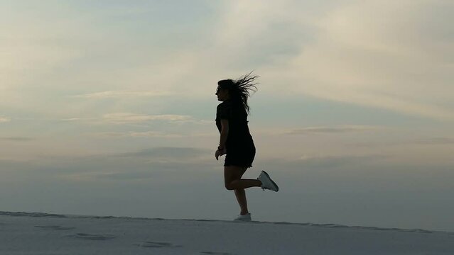 Slow motion footage silhouette of a girl running in the desert. A brunette in a black short dress running in the desert at sunset against a clear sky. Feeling of Freedom, Concept.