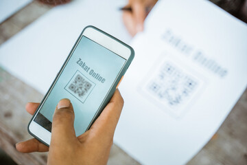 close up of hand paying zakat online using mobile phone and scanning payment barcode