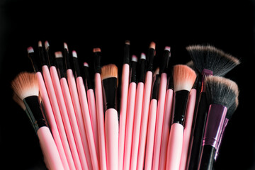 Pink face makeup brushes on a black acrylic background with a reflection of themselves.