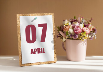 April 7. 7th day of month, calendar date.Bouquet of dead wood in pink mug on desktop.Cork board with calendar sheet on white-beige background. Concept of day of year, time planner, spring month