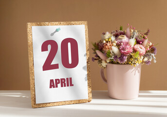 April 20. 20th day of month, calendar date.Bouquet of dead wood in pink mug on desktop.Cork board...