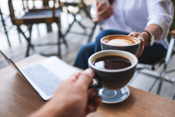 Closeup image of two businessman clinking coffee cups together while working and meeting with laptop computer on the table