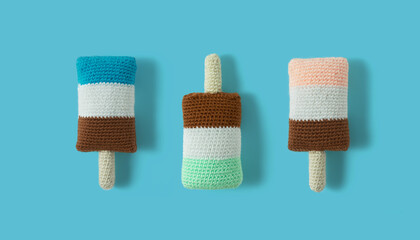 Ice cream popsicle pattern knitted with colored yarn. Handmade knitted products in the form of ice cream. Sweet, juicy, fresh popsicles on pastel blue background. Top view