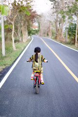 Blurred back of asian little child girl try to riding a bicycle on asphalt road background