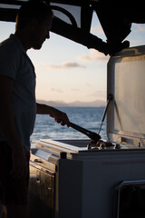 caucasian man shillouette cooking BBQ sunset boat ocean holiday vacation relax food eat 