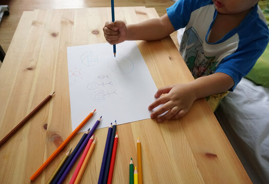 Cute Asian boy drawing happy family and home. with color pencils and white paper on wooden table