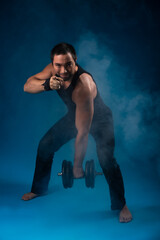 Obraz premium muscular man with dumbbells. sportsman posing in black t-shirt, jeans with dumbbells. studio portrait. blue background