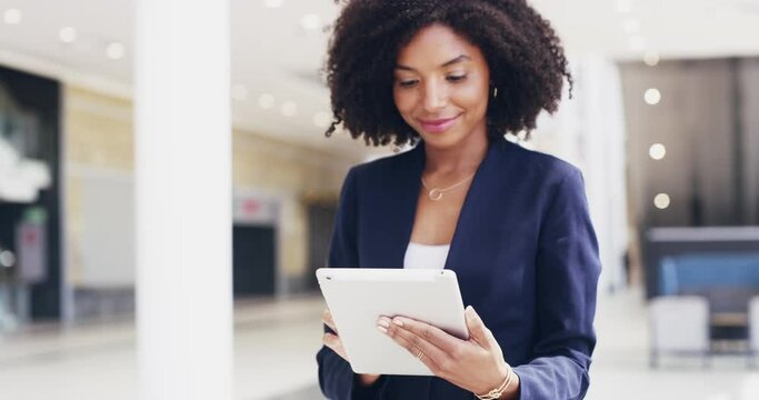 Inspiration is not hard to find online. Beautiful happy confident young multi ethnic business woman with afro walking through a modern office alone and using a digital tablet to finish work