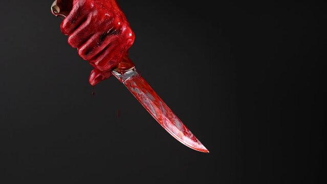 Man holding knife with bloody hand on black background. 