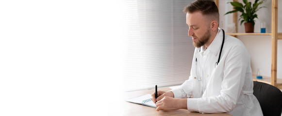 side view of a male doctor in the office in a white coat with a stethoscope working at the table. A...