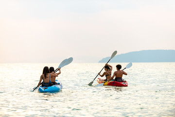 Group of young Asian man and woman kayaking in the sea together at tropical island on summer vacation. Happy male and female friends enjoy outdoor lifestyle and water sports on beach holiday vacation