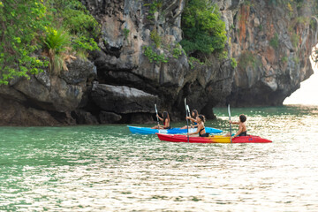 Fototapeta na wymiar Group of young Asian man and woman kayaking in the sea together at tropical island on summer vacation. Happy male and female friends enjoy outdoor lifestyle and water sports on beach holiday vacation