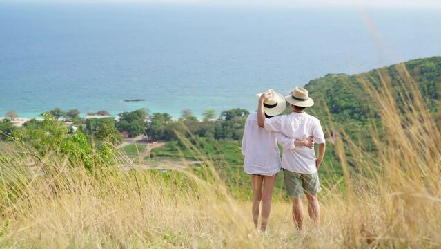 4K Happy Asian family couple walking with embracing each other while travel together on tropical island mountain in summer sunny day. Husband and wife enjoy outdoor lifestyle holiday travel vacation