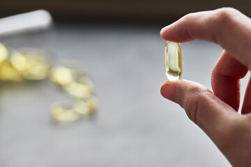A person holds an omega-3 fatty acid capsule against a gray background. The concept of medicine and healthy living. Front view.