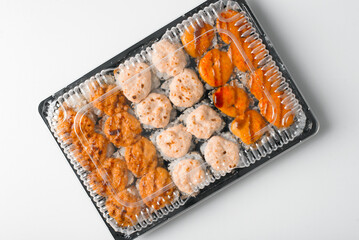 Delivery baked hot rolls set in plastic container on white table. Japanese traditional food, Asian cuisine. Top view, close-up