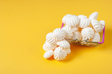 French Meringue dessert in a children's shopping basket on a yellow background. Meringue is made from a mixture of beaten egg whites with sugar.