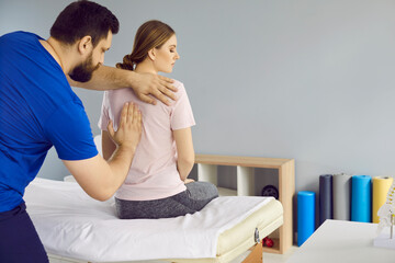 Osteopathic medicine and physiotherapy. Professional chiropractor treats young woman's back pain in modern medical clinic. Male doctor fixes back muscles in woman sitting on couch in hospital room. - obrazy, fototapety, plakaty
