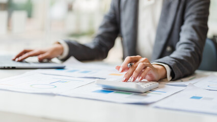 Close up woman hands using calculator and laptop at desk in modern office, accountant and tax concept.