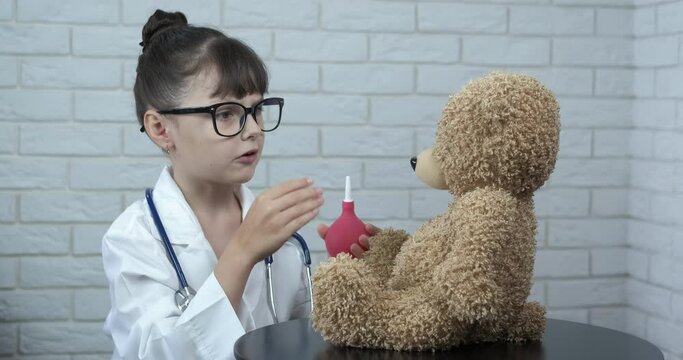 The child plays doctor. Treat plush toy. A little girl in medical uniform try to cure her plush toy with an enema in the cabinet.