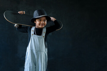 Portrait of smiling African American little kid boy holds a skateboard on his shoulders on black...