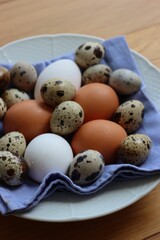 Fresh chicken brown and white eggs and quail eggs in a bowl on wooden table