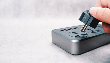 A human hand inserting a plug into a power outlet on the cement floor with copy space