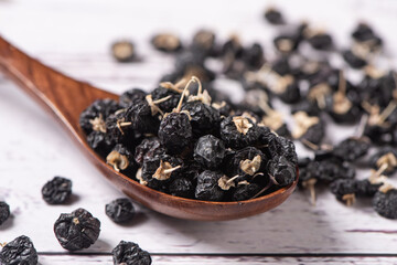 Black wolfberries in a wooden spoon on table.
