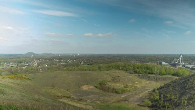 Old mining heap and quarry overgrown with green grass. Mining tower in horizon, time lapse view