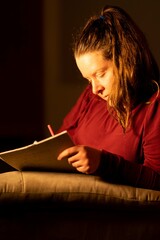beautiful elegant smart woman writing down her ideas in a diary. Smiling brunette lady with notebook and pen in her hands. Modern dark home interior on background, at night