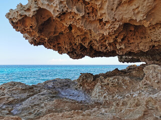 A stone, a rock, a hanging piece of long-frozen lava, below dried salt, similar to ice, against the background of the sea and a blue cloudless sky.