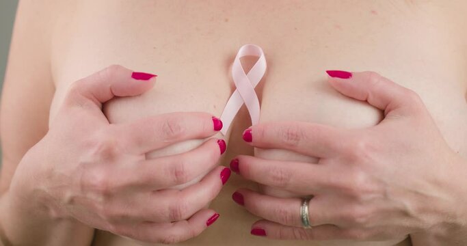 Naked woman covering her breasts with her hands with breast cancer symbol between.