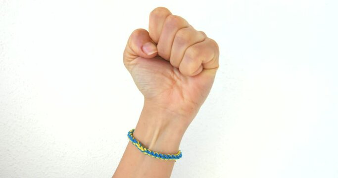 Clenching Fist With Ukrainian Symbol Knitted Bracelet On Wrist Raised On White Background. - Closeup