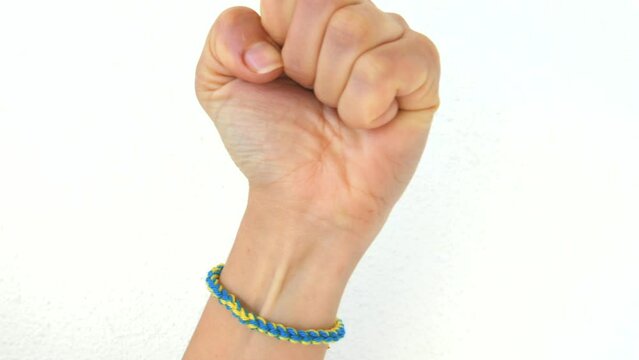 Clenched Fist Showing Support To Ukraine With A Wristband Of Blue And Yellow Colors Isolated Against White Background. - Closeup