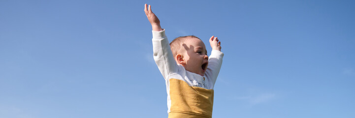 Happy little boy enjoying nature outdoors with arms raised.